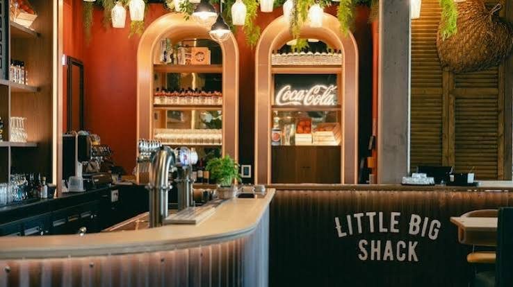 Le bar du Little Big Shack, arches en bois clair et enseigne peinte sur le comptoir.