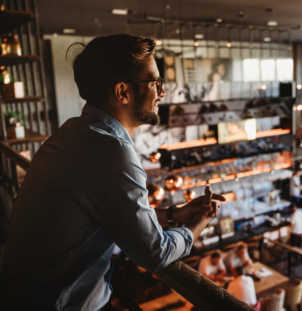Un restaurateur accoudé à la rambarde de sa mezzanine, observant sa salle en service.